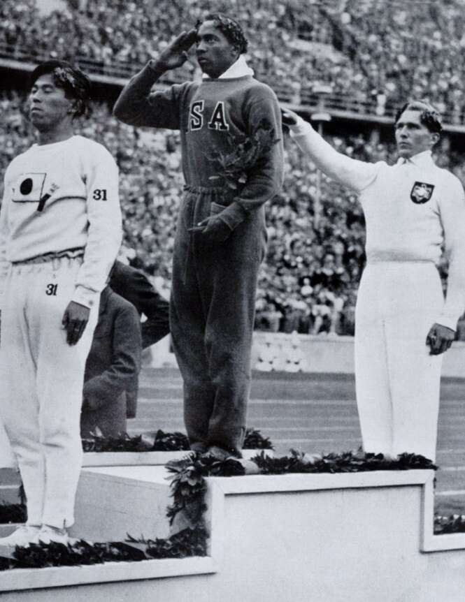 Sport. 1936 Olympic Games in Berlin. Mens Long Jump. Medal Ceremony. USA's Jesse Owens, centre, salutes the flag after winning the Gold medal, with left, Naoto Tajima, Japan (Bronze medal), right, Lutz Long, Germany, (silver  medal).